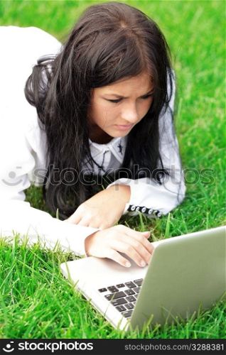 Young woman working on laptop. Lying on green lawn