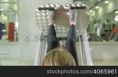 Young woman working out in health fitness club on leg press machine, closeup rear view jib crane shot
