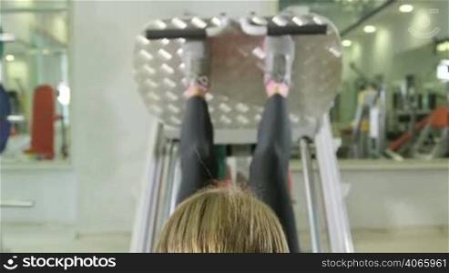 Young woman working out in health fitness club on leg press machine, closeup rear view jib crane shot