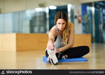Young woman working out indoors. Female stretching their legs on the floor of a gym.