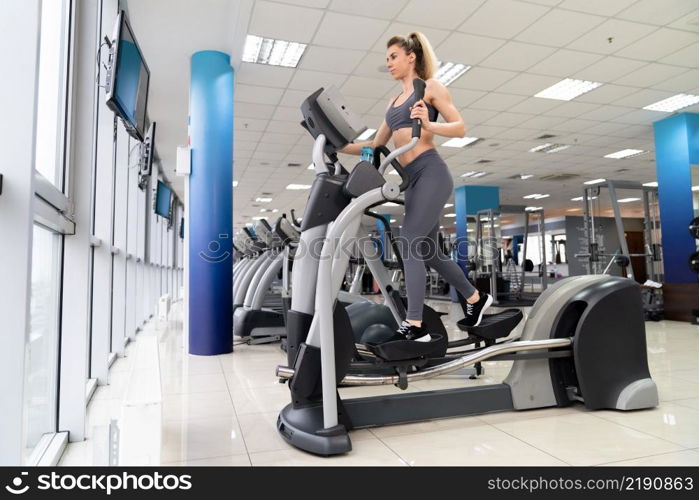 Young woman working out on orbi track at gym exercising inside fitness center. Young woman working out on orbi track at gym exercising