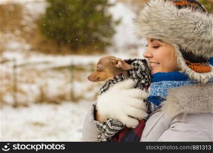 Young woman wrapped her best friend little dog in warm blanket scarf to warm him in cold snowy winter day. Animal protection save. Adoption concept. Woman hug warming her little dog in winter