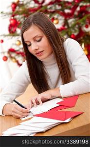 Young woman writing Christmas card in front of tree