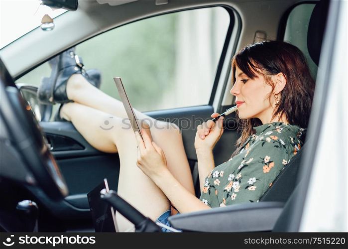 Young woman writing in a notebook with a pen in a white car pulling her feet out the window. Female wearing flowered shirt and shorts.. Woman writing in a notebook with a pen in a white car