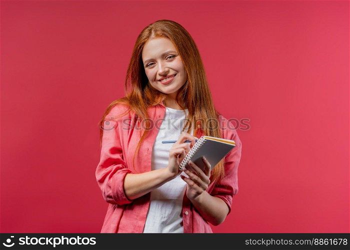 Young woman writing notes in planner with pen. Student girl thinking about future plans and to-do list in notebook for week, month, year. Keeping personal diary on pink background. High quality photo. Young woman writing notes in planner with pen. Student girl thinking about future plans and to-do list in notebook for week, month, year. Keeping personal diary on pink background.