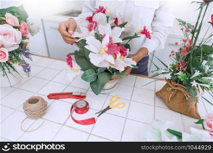 young women business owner florist making or Arranging Artificial flowers vest in her shop, craft and hand made concept.