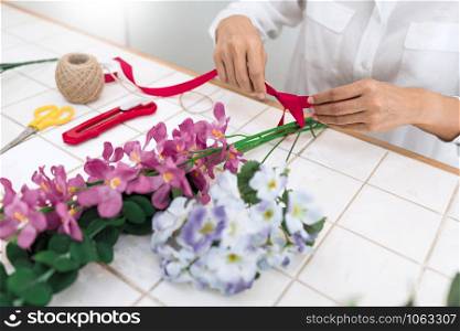 young women business owner florist making or Arranging Artificial flowers vest in her shop, craft and hand made concept.