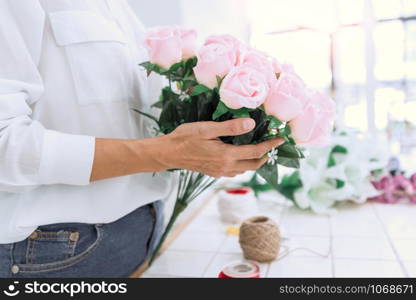 young women business owner florist making or Arranging Artificial flowers vest in her shop, craft and hand made concept.