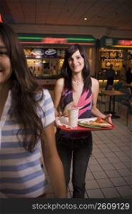 Young women carrying trays in mall food court