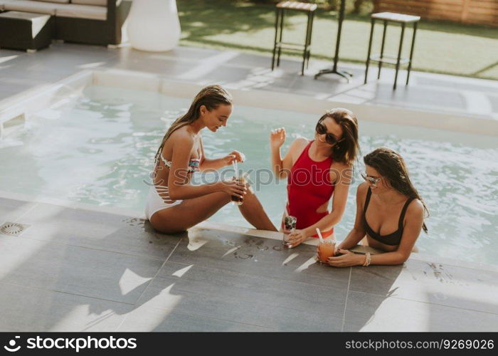 Young women drinking coctail and having fun by swimming pool at hot summer day