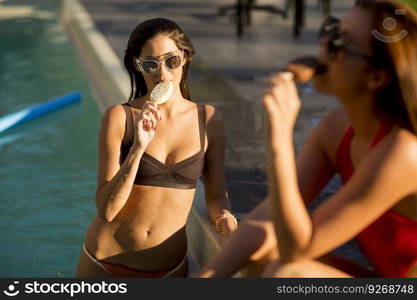 Young women eating ice cream by the swimming pool