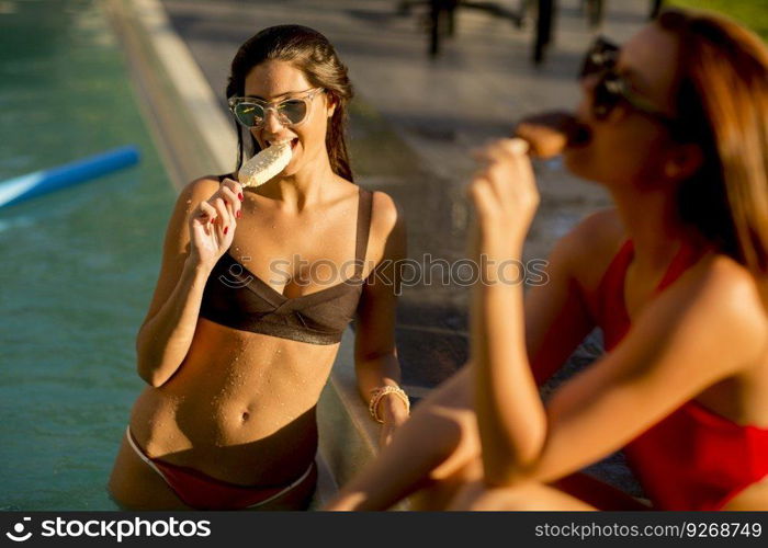 Young women eating ice cream by the swimming pool