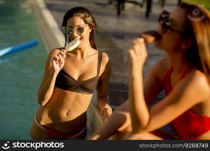 Young women eating ice cream by the swimming pool