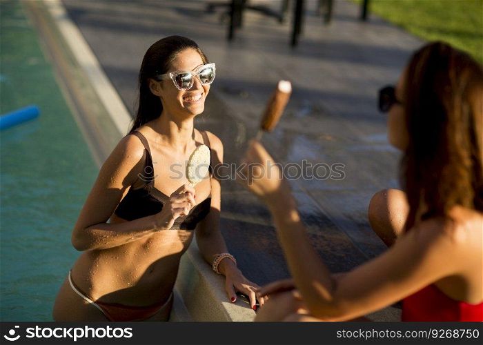 Young women eating ice cream by the swimming pool