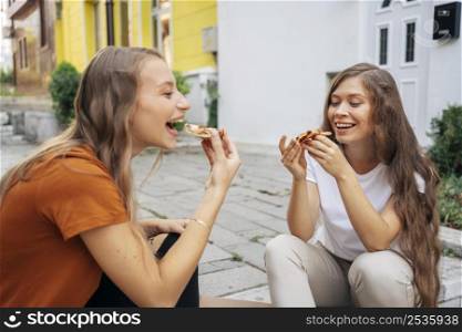 young women eating pizza together outdoors