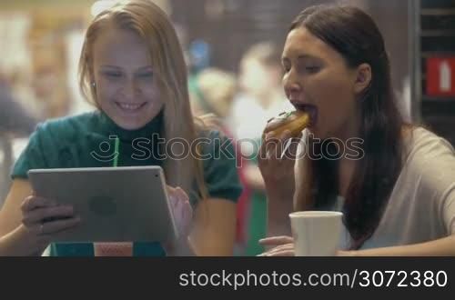 Young women enjoying the evening in cafe while it raining outside. They using touch pad, drinking coffee and eating together one delicious cake