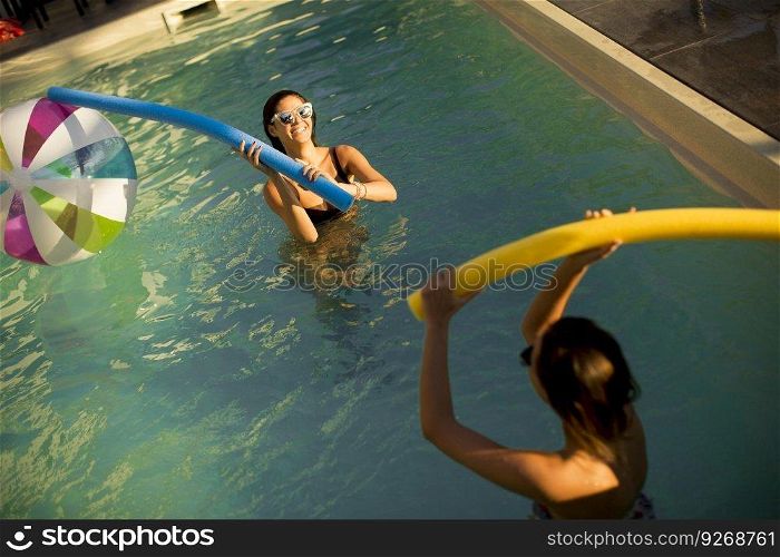 Young women having fun with swimming pool noodles at hot summer day