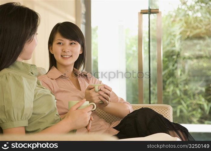 Young women holding coffee cups and looking at each other