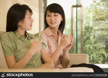 Young women holding coffee cups and looking at each other