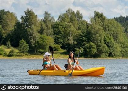 Young women in bikinis kayaking on river summertime
