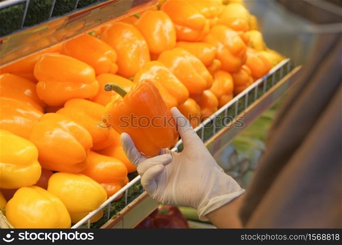 young women in protective gloves holding capsicum at retail store.. young women in protective gloves holding capsicum at retail store