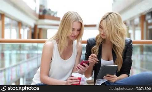Young women in shopping mall using digital tablet and smartphone