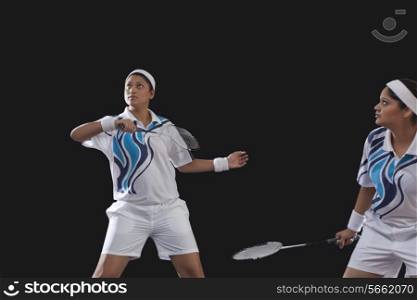 Young women in sportswear playing badminton against black background
