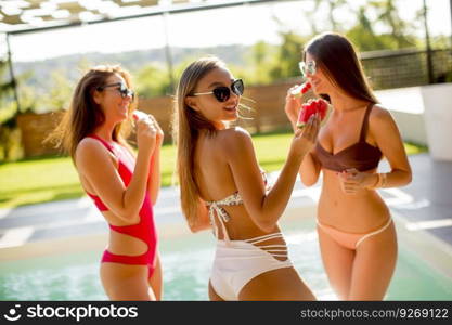 Young women in swimsuit eating watermelon by pool at hot summer day