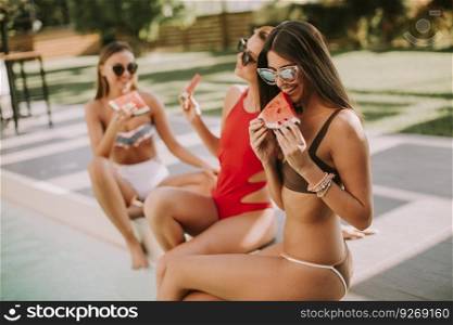 Young women in swimsuit eating watermelon by pool at hot summer day