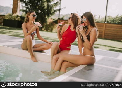 Young women in swimsuit eating watermelon by pool at hot summer day