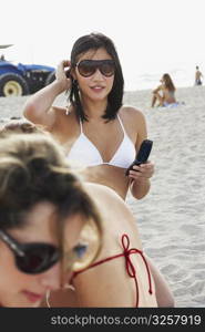 Young women listening to music and talking on cell phone while sunbathing on beach