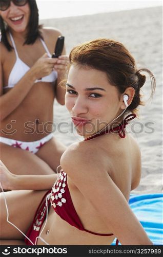 Young women listening to music and talking on cell phone while sunbathing on beach