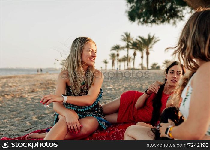 Young women lying on beach, smiling and talking over big scarf