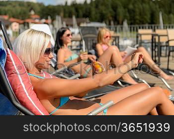 Young women lying on deckchair applying sunscreen in bikini