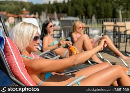 Young women lying on deckchair applying sunscreen in bikini