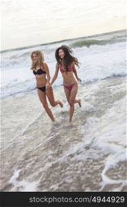 Young women or girls in bikinis running in the sea waves on a beach