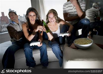 Young women playing a video game and toasting with beer bottles