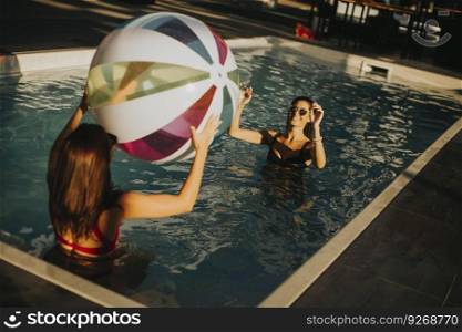 Young women playing with a ball in the swimming pool at sunny day