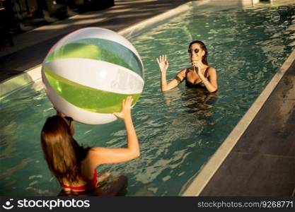 Young women playing with a ball in the swimming pool at sunny day