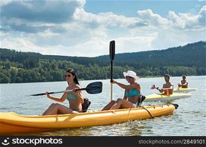 Young women rowing on kayaks with friends summertime