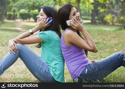 Young women sitting back to back while talking on cell phone