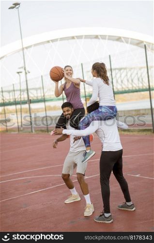 Young women sitting on the men shoulders and holding a basketball at outdoor court on a sunny day