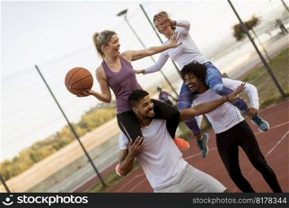 Young women sitting on the men shoulders and holding a basketball at outdoor court on a sunny day