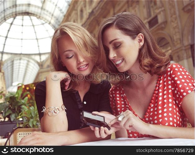 young women smiling and laughing as they look at text message on mobile phone