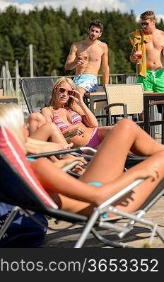 Young women sunbathing on deckchair and guys drinking beer