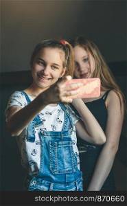 Young women taking selfie, using smartphone camera. Girls making faces, enjoying taking funny pictures together
