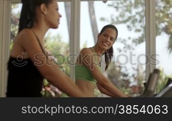 Young women talking and laughing while working out on exercise bicycles in wellness club