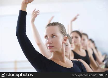 Young women with arms raised at the barre