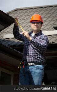 Young worker in hard hat measuring size of house roof