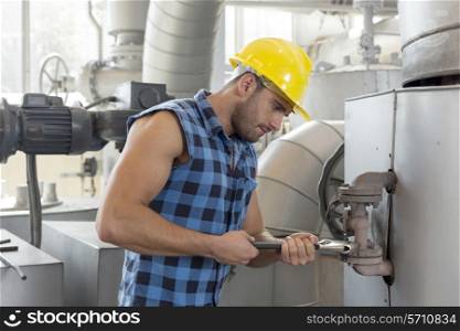 Young worker using wrench on industrial machine